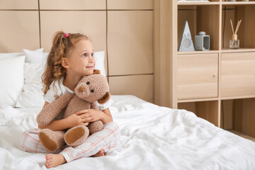 Adorable little girl with teddy bear in bedroom