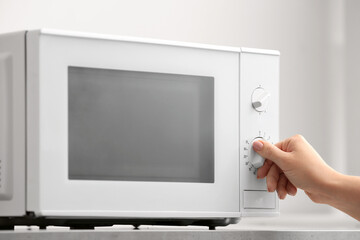 Woman warming food in microwave oven on light background, closeup