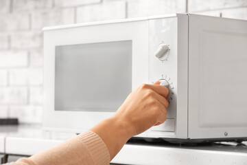 Woman warming food in modern microwave oven on table against brick wall background, closeup