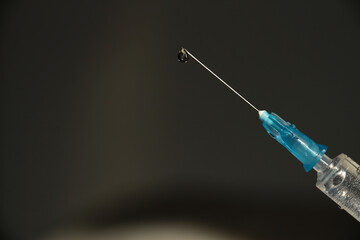 Syringe with a needle for injection with a drop, close-up on a dark background. Space for your text