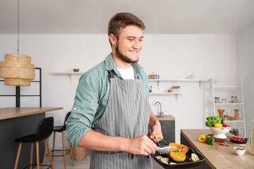 Young man holding frying pan with vegetables in kitchen