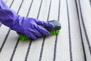 Woman in rubber glove cleaning striped carpet with brush at home, closeup