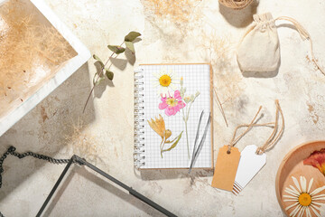 Composition with dried pressed flowers, notebook and blank tags on light background