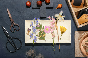 Composition with dried pressed flowers and scissors on black background