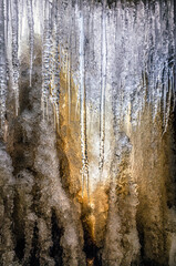 Photographed from behind a frozen waterfall, light shines through a wall of ice illuminating hanging icicles at Upper Cataract Falls in Indiana during a winter cold spell.