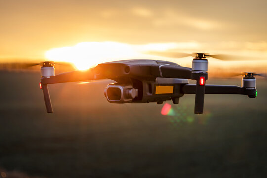 Unmanned quadcopter in flight with a digital camera at sunset. Drone silhouette at sunset