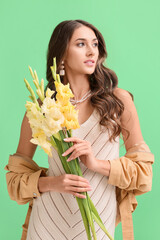Elegant woman with bouquet of Gladiolus flowers looking away on green background