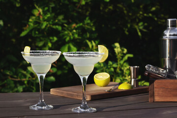 Two glasses with fresh homemade margarita cocktail on a wooden table on a patio summer evening, selective focus