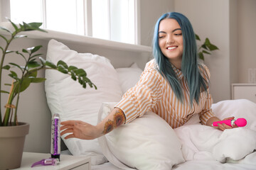 Beautiful young woman taking vibrator from bedside table - obrazy, fototapety, plakaty