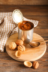 Tin can with boiled condensed milk and tasty walnut shaped cookies on wooden background