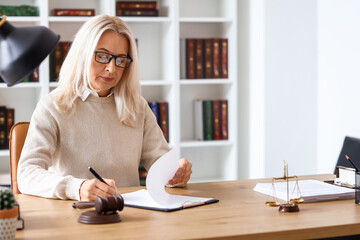 Mature female judge working with document at table in courtroom