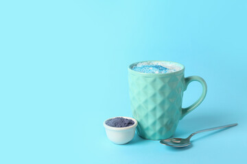 Cup of blue matcha latte and bowl with powder on color background