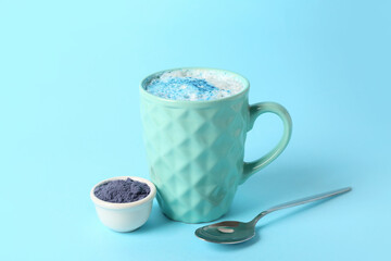 Cup of blue matcha latte and bowl with powder on color background