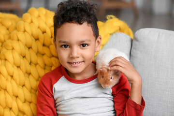 Little African-American boy with cute guinea pig on sofa at home