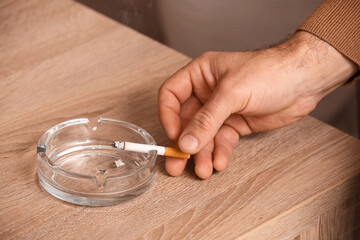 Smoking man using ash tray at home, closeup