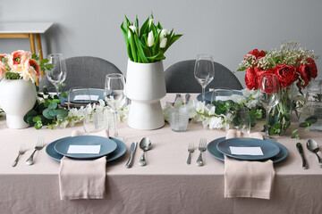 Stylish table setting with tulip flowers near grey wall