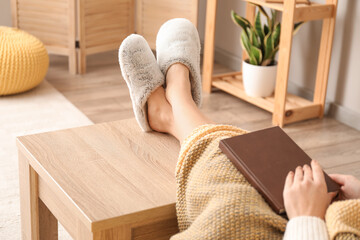 Young woman in soft comfortable slippers reading book at home