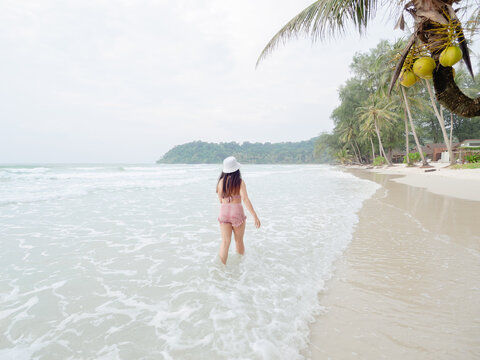 Hipster young woman in bikini walking barefoot on the beach and look to the little waves. summer concept.