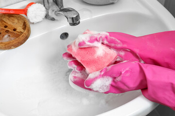 Woman with sponge cleaning ceramic sink in bathroom, closeup