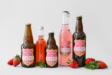 Bottles of fresh strawberry kombucha on light background