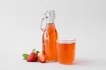 Bottle and glass of fresh strawberry kombucha on light background
