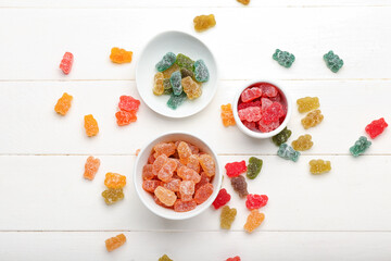Bowls with different jelly bears on white wooden background