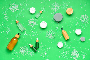 Different cosmetic products and snowflakes on green background