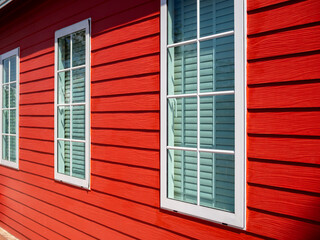 Three simple white closed windows with glass and louver decoration on the red wooden plank wall, residential, view from outdoor.