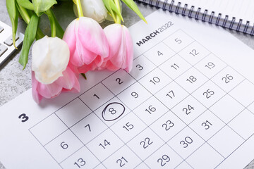 Calendar and flowers for International Women's Day celebration on table, closeup
