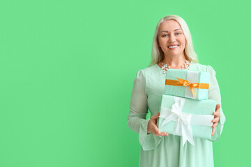 Fashionable mature woman holding stack of gift boxes on green background. International Women's Day celebration