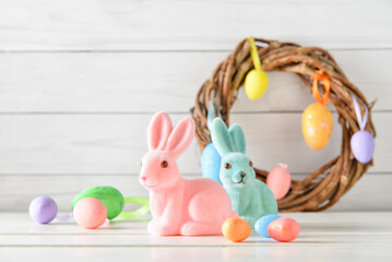 Easter bunnies, painted eggs and wreath on white wooden background