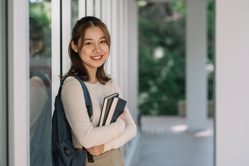 Cute Asian female student standing holding a book looking at the camera. - Powered by Adobe