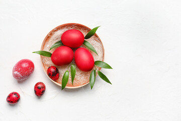 Plate with red painted Easter eggs and green leaves on light background