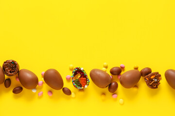 Composition with chocolate Easter eggs and candies on yellow background