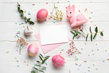 Beautiful Easter composition with blank card, painted eggs, bunny and flowers on light wooden background