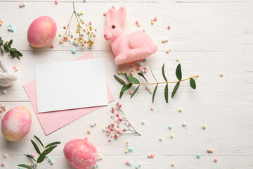Beautiful Easter composition with blank card, painted eggs, bunny and flowers on light wooden background