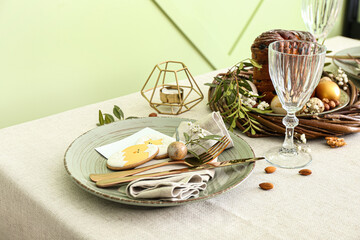 Dining table with beautiful setting for Easter celebration with cookies near green wall