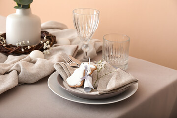 Dining table for Easter celebration with cookie in shape of bunny near beige wall