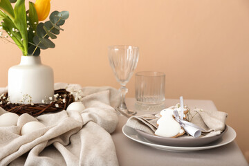 Dining table for Easter celebration with cookie in shape of bunny near beige wall