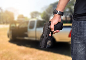 Semi-automatic black 9mm pistol gun holding in hands of gun shooter with blurred pickup car in the afternoon background, concept for car robbery, bodyguard, vip protection, gangsters and mafias