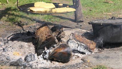 Baking bread on a griddle over a fire outdoors in 1800's America