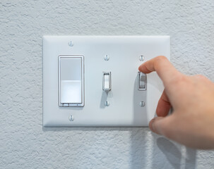 Closeup hand turning on-off switch after using, saving energy concept. Minimal design of mounted electricity control on the wall. Household electric outlet in home, residential, indoor room, apartment