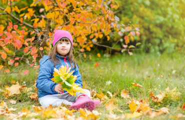 Happy young girl with down syndrome sitting on autumn leaves. Empty space for text