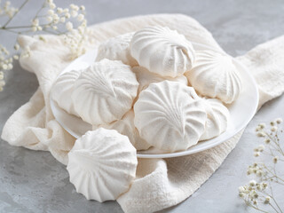 Airy Russian marshmallow dessert zephyr. Meringue dessert on a white plate next to flowers. Selective focus. Light background.
