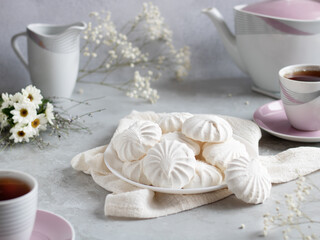 Airy Russian marshmallow dessert zephyr. Meringue dessert on a white plate next to a tea set and flowers. Selective focus. Light background.