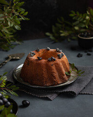 Round bundt cake with raisins, close-up. Bundt Cake with raisins. Selective focus, Shallow Depth of Field, Close up. Clusters of grapes and branches in the background and foreground.