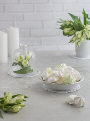 Marshmallow dessert. Meringue dessert on a white plate next to flowers and candles. Selective focus. Light background.
