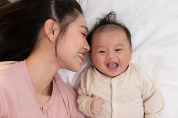New asian mom playing to adorable newborn baby on bed smiling and happiness at home.Mom talking with infant baby and kissing on baby cheek with love.Baby and Mother day concept