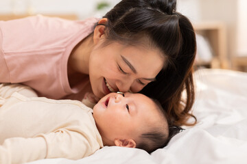 New asian mom playing to adorable newborn baby on bed smiling and happiness at home.Mom talking with infant baby and kissing on baby cheek with love.Baby and Mother day concept