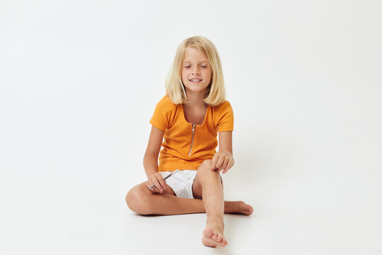 a cheerful little girl in a yellow t-shirt sits on the floor with her legs folded